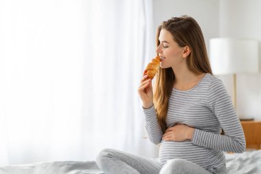 Hamile bir kadın, Avrupa 'daki evinde hamilelik bakımıyla zevki dengeleyen lezzetli bir kruvasan yiyor.