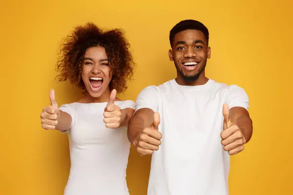 We love it. Emotional african man and woman gesturing thumbs up on orange studio background