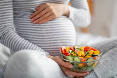 Avrupalı hamile bir kadın besleyici bir salata yerken bir anlık sükunet içinde yakalanıyor ve evde hamilelik sırasında sağlıklı beslenmenin önemini vurguluyor.