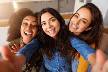 Neşeli, çok kültürlü genç kadınlar evde bir selfie anı yakalıyorlar, sıcak dostluk ve gülümseme sergiliyorlar.