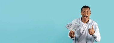 Heyecanlı bir adam mavi model arka planda cömert boşluğun yanında bir avuç dolusu para sergiliyor.