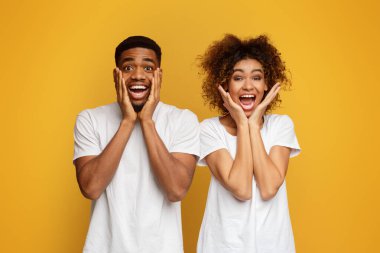 Afro-Amerikalı kadın ve erkek kameraya sevinçle bakar, yanaklara dokunur, olumlu duygular ve şaşkınlığı ifade eder, turuncu arka plan