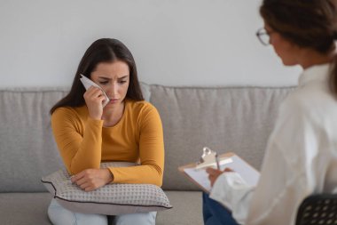 Kasvetli bir ruh hali içinde genç bir kadın terapi seansını anlatan notlar alan bir terapistle görüşüyor.