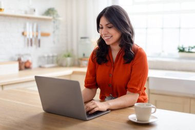 Ortadoğulu bir kadın evinde rahat bir şekilde oturup dizüstü bilgisayarıyla meşgul oluyor. Yakınlaştırma teknolojisini temsil eden mutlu bir ifadesi var.