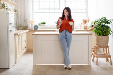 Pozitif Ortadoğulu kadın kahve içiyor, akıllı telefon kullanıyor, mutfak tezgahının yanında duruyor, fotokopi odası var.