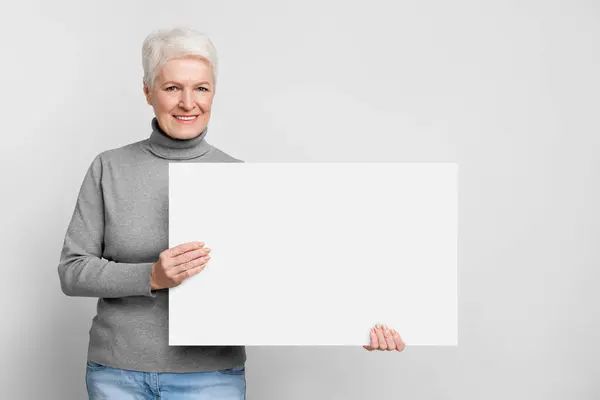 Elderly European Woman Presents Blank Board Gentle Smile Promoting S3Niorlife — Stock Photo, Image