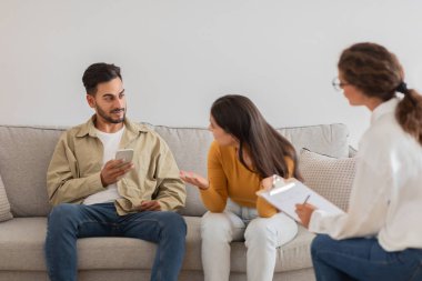Genç bir çiftin, aile seansı sırasında akıllı telefonuyla dikkati dağılır. Bu da evliliğindeki bir sorunu gösterebilir.