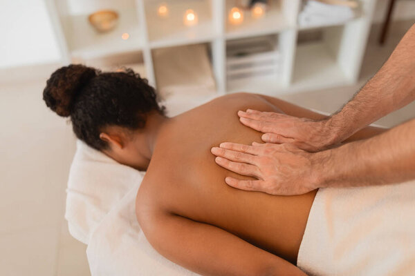 Masseur applies focused pressure on African American womans back during a therapeutic session in a tranquil spa