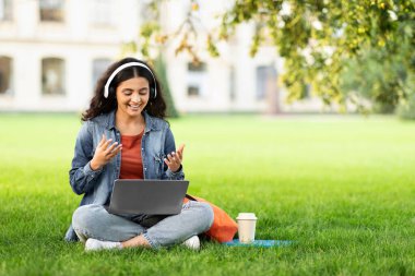 Hindu lady student engaging in a video call on her laptop in a park, representing technology in education clipart