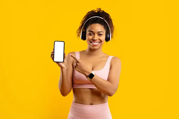 Czarny Fitness Pani Prezentuje Smartfon Pustym Ekranem Kciuki Góry Słuchawki Obrazy Stockowe bez tantiem