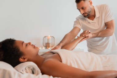 Barışçıl bir spa ortamında profesyonel bir masör, siyah bir bayana bakar, sağlığına ve kaplıca tedavilerinin insan eli değmesine odaklanır.