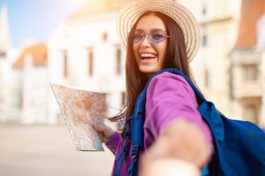 Elinde bir haritayla, bin yıllık bir bayan dışarıda heyecan gösteriyor. Avrupa kentsel ortamında davetkar bir jest yapıyor.