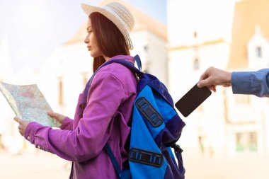 Young woman tourist focusing on a map is unaware as a thiefs hand reaches for her phone in an urban setting clipart