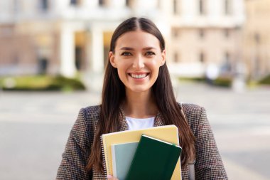 Gülümseyen bir milenyum bayanı tasviri, elinde not defterleri olan bir öğrenci gibi giyinmiş, Avrupa kentsel ortamında.
