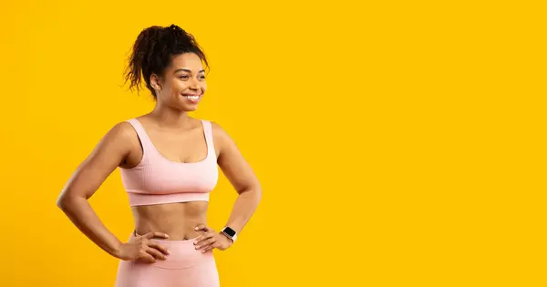 一位容光焕发的非洲裔美国女士 面带微笑 自信地穿着健美的衣服 面对着孤立的黄色背景 — 图库照片