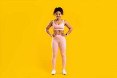 Fit african american woman stands smiling in sporty attire, isolated on a vibrant yellow background clipart