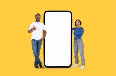Mutlu bir siyah erkek ve kadın, sarı bir arka planda, büyük, boş bir akıllı telefon ekranının yanında duruyor. Reklam içeriği için ideal.