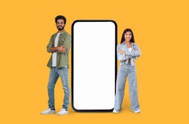 Orta Doğulu genç çift, sarı arkaplanda dev bir akıllı telefon illüstrasyonuyla gülümsüyor.