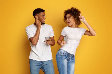 Neşeli bin yıllık siyah erkek ve kadın cep telefonları müzik dinleme ve her diğer, turuncu arka plana gülümseyen kulaklık