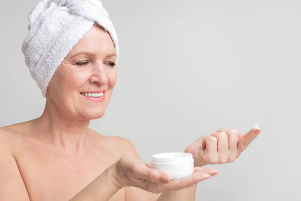 一位年长的欧洲裔女士展示了一种带有面霜的自我护理程序 记录了她一生中致力于护肤的一刻 — 图库照片