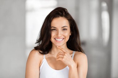 Neşeli genç bir kadın, ışıl ışıl gülümseyen, kendine güvenen, bulanık bir arka planla kameraya bakan