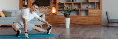 Bacaklar için egzersiz yapan, oturma odasının iç tarafındaki spor minderinde uzanan ve kameraya gülümseyen olgun sporcu. Evde eğitim, egzersiz, spor ve kilo kaybı, kopyalama alanı