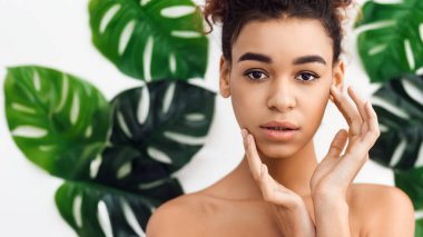 Çevresi yeşil yapraklarla çevrili, sakin bir ifadeyle içsel Afro-Amerikan kadın spa ve bütünsel sağlık temasını çağrıştırıyor.