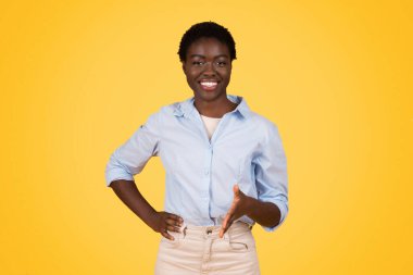 A confident young african american woman smiling at the camera with her hands on her hips against a yellow background, exuding positivity and confidence clipart