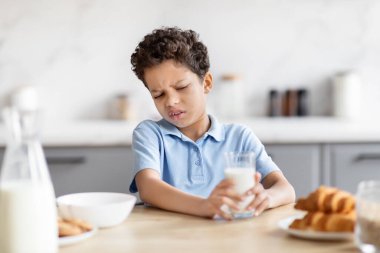 Fotoğrafta, elinde bir bardak süt tutarken, bir mutfaktaki hoşnutsuzluğu veya diyet rahatsızlığını gösteren gözle görülür derecede tatsız bir tepki veren Afro-Amerikalı bir çocuk görülüyor.