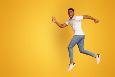 Turuncu studio arka planda, kameraya gülümseyen atlama havada, yürüyüş neşeli bin yıllık Afrikalı-Amerikalı adam