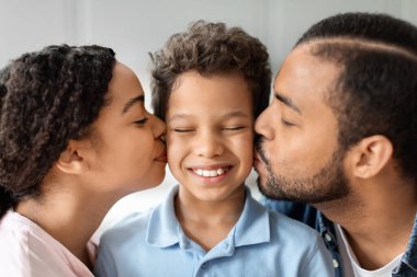 Afro-Amerikan ailesi, çocuklarına öpücük verirken, neşeyi, siyahları ve aile bağlarını vurgulayarak, sevgi dolu bir anı paylaşıyor.