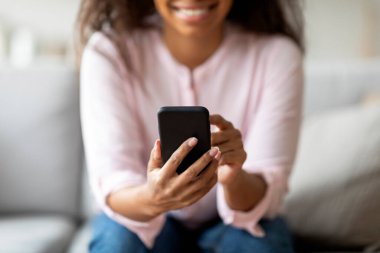 Evde Afro-Amerikalı bir kadın telefonuna mesaj yolluyor. Bulanık bir yüzle iletişim kurma eylemine odaklanıyor.