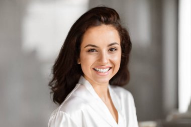 Işıl ışıl bir kadın banyoda cilt bakımı rutini yaparken gülümsüyor, bin yıllık cilt bakımı ve pozitifliği özetliyor.