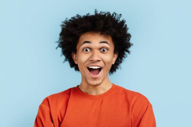 An exuberant black guy laughing heartily, wearing an orange sweater, conveying infectious joy against a blue isolated background. Perfect for depicting genuine happiness clipart