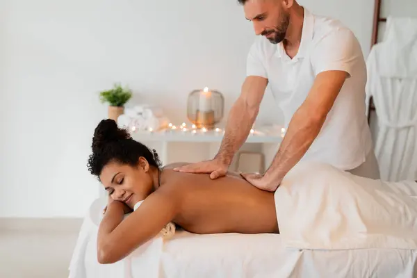 stock image A skilled masseur administers a relaxing back massage to an african american lady at a modern spa, emphasizing human touch and professional care