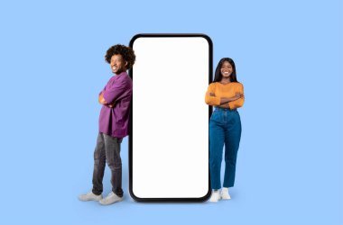 Rahat Afro-Amerikan erkek ve kadın rahat giyiniyor mavi arka planda büyük bir akıllı telefonun yanında, taklit kopya alanı