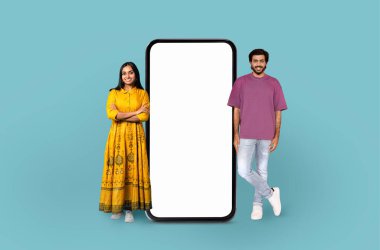 Geleneksel giysili Hintli kadın ve günlük giysili bir adam büyük bir akıllı telefon ekranının yanında duruyor.
