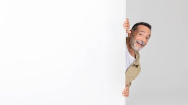 A senior man is cautiously peeking out from behind a white wall, his eyes scanning the area. The wall provides partial cover as he observes his surroundings. clipart