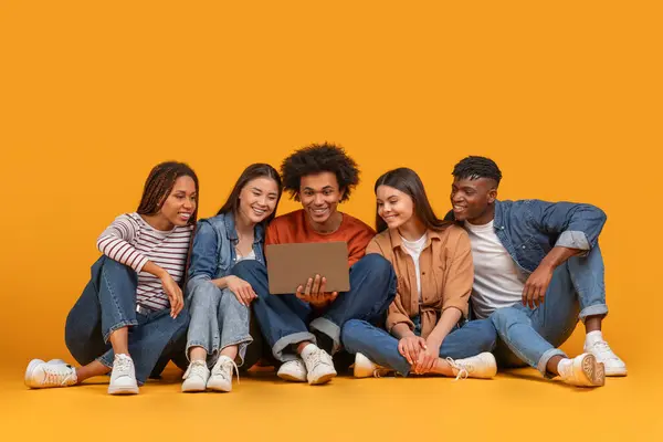 stock image A connected team of young multiethnic friends engaging with a laptop, symbolizing technology in a friendship context, isolated on a yellow background