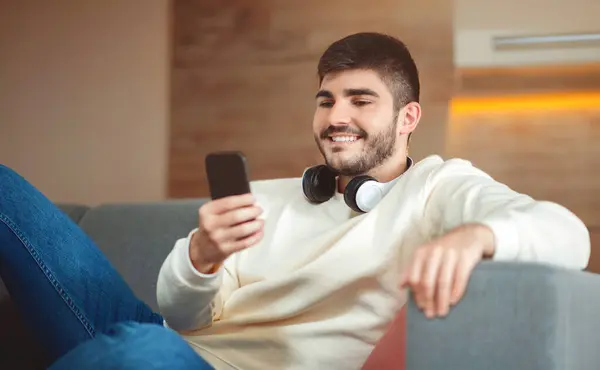 Homem Feliz Está Sentado Sofá Dentro Casa Segurando Telefone Inteligente — Fotografia de Stock