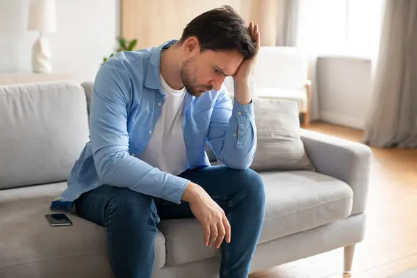 Man Sitting Couch Holding His Head Both Hands Appears Deep — Stock Photo, Image
