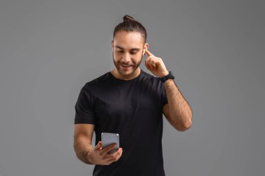 Dışarıda dikilen, elinde cep telefonu olan ve kulağına kulaklık takan bir adam..