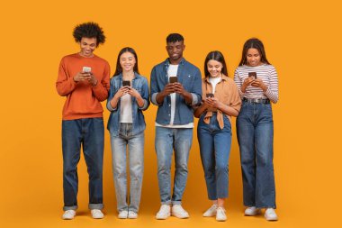 An international group of young friends absorbed in their smartphones, embodying multiethnic, multiracial connectivity in a digital age, isolated on orange clipart