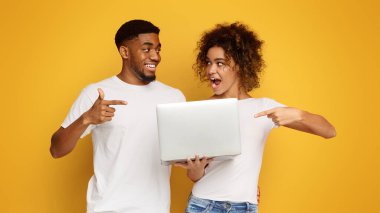 Neşeli milenyal siyah adam ve kadın laptop işaret, Web sitesi gibi, turuncu arka plan