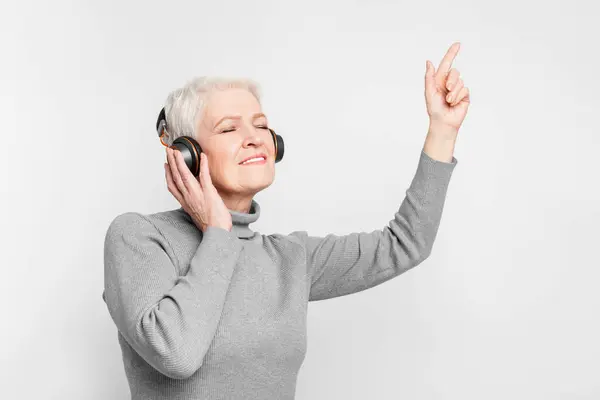 タートルネックの年配のヨーロッパ人女性がヘッドホンで音楽を聴きながら笑顔を浮かべ 楽しいS3Niorlifeを表しています ストック画像