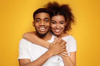 Birbirine aşık bir çift. Genç ve sevimli Afro-Amerikan çift kucaklaşıyorlar, turuncu arka planda poz veriyorlar, fotokopi alanı.