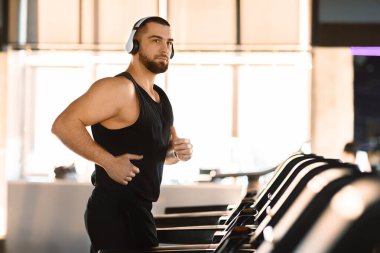 Kulaklıklı odaklanmış bir adam koşu bandında koşuyor, spor salonundaki spor salonuna bağlılığını gösteriyor.
