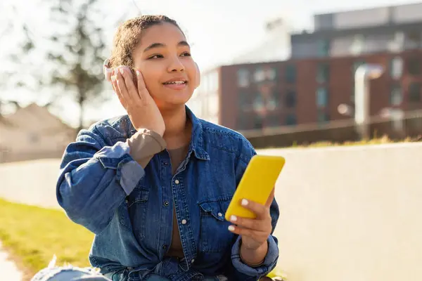 Młoda Dziewczyna Słuchawkami Siedzi Ziemi Pochłonięta Telefonem Komórkowym Jej Uwaga — Zdjęcie stockowe