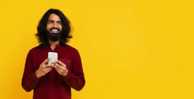 Uzun saçlı ve sakallı Hintli bir adam elinde bir cep telefonu tutuyor. Ekrana odaklanmış gibi görünüyor, belki mesaj ya da tarama, boşluğu kopyalama