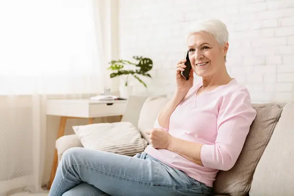 年配の女性が彼女の携帯電話で話して コピー スペースのソファで休んで ストック画像